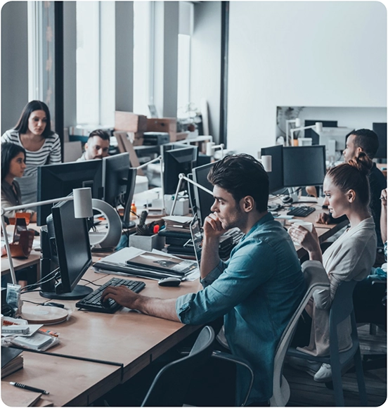 Group of people working at computers in an open office space.